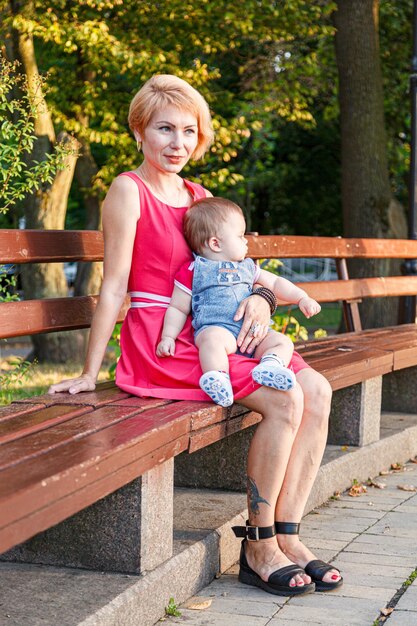 Piękna mama z córką i synem siedzą latem na ławce w parku