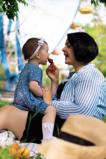 Piękna matka i jej urocza córka jedzą truskawki i mandarynki w parku