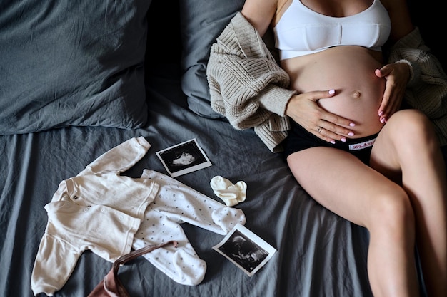 Zdjęcie piękna matka w ciąży z białymi ubrankami dla dzieci kobieta w ciąży pakująca torbę szpitalną dla kobiet w ciąży koncepcja ciąża ciąża poród