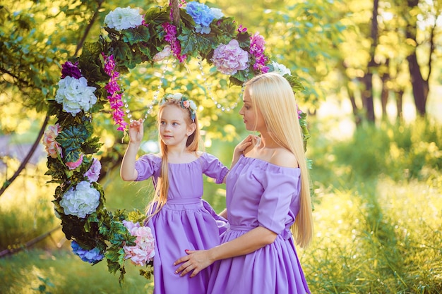 Piękna Matka Z Długimi Blond Włosami, Pozowanie I Zabawy Z Córką W Podobnych Lawendowych Sukienkach W Parku Na świeżym Powietrzu
