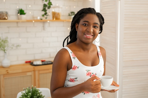 piękna młoda afrykańska kobieta w letniej sukience w kuchni, picie herbaty