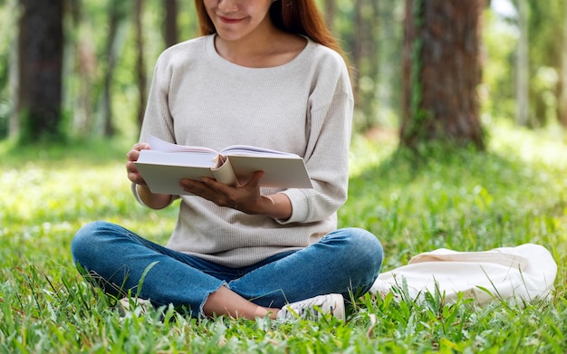 Piękna młoda Azjatka czytająca książkę siedząc w parku