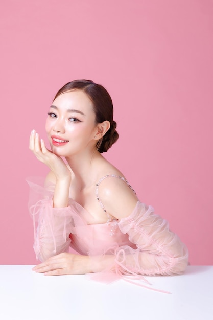 Piękna młoda Azjatka modelka włosów z naturalnym makijażem na twarzy czysta świeża skóra na izolowanym różowym tle Piękny portret dziewczyny Leczenie twarzy koncepcja Walentynki