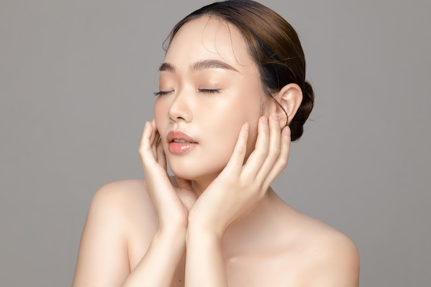 Piękna młoda Azjatycka kobieta model z idealnie czystą świeżą skórą na szarym tle Pielęgnacja twarzy Zabieg na twarz Kosmetologia Chirurgia plastyczna Piękny portret dziewczyny w studio