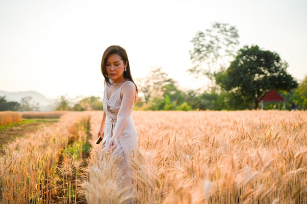 Piękna młoda azjatycka kobieta stojąca na polu pszenicy jęczmiennej przed światłem słonecznym