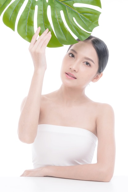 Piękna młoda Azjatycka kobieta z czystą skórą, świeżą skórą trzymającą zielony tropikalny liść w dłoniach na białym tle - strzał piękności azjatyckiej kobiety Zabieg na twarz, kosmetologia, uroda i koncepcja spa