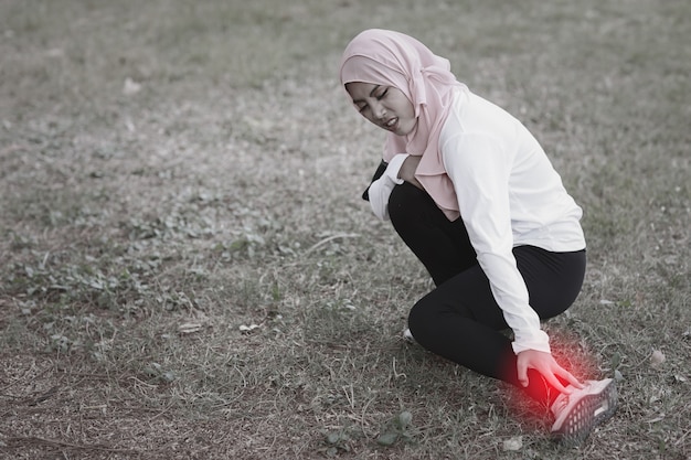 Piękna Młoda Azjatycka Muzułmańska Dziewczyna W Sportowej Trzyma Ręce Na Nodze I Ból Po Długim Treningu. Fitness Kobieta Ma Problem Lub Wypadek Podczas Treningu. Koncepcja Medyczna I Sportowa