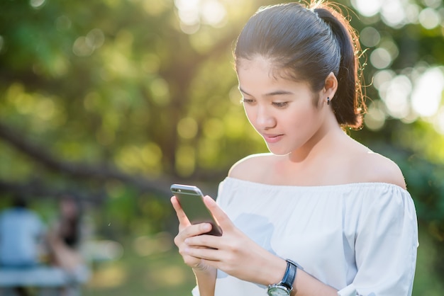 Zdjęcie piękna młoda azjatykcia kobieta ono uśmiecha się podczas gdy czytający jej smartphone w ogródzie.