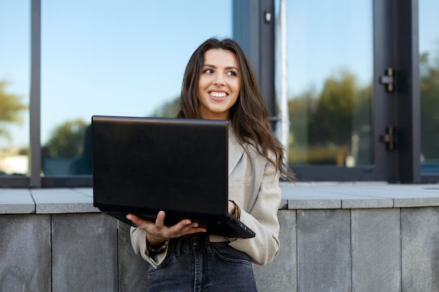 Piękna młoda bizneswoman za pomocą laptopa na zewnątrz, studiując online, pracując w Internecie