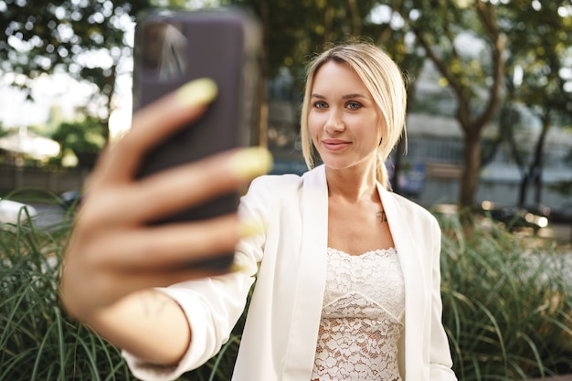 Piękna młoda blond bizneswoman za pomocą smartfona w mieście