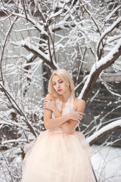 Piękna młoda blond kobieta w białej sukni pozuje w snowy winter park. Nieostrość. Selektywne skupienie