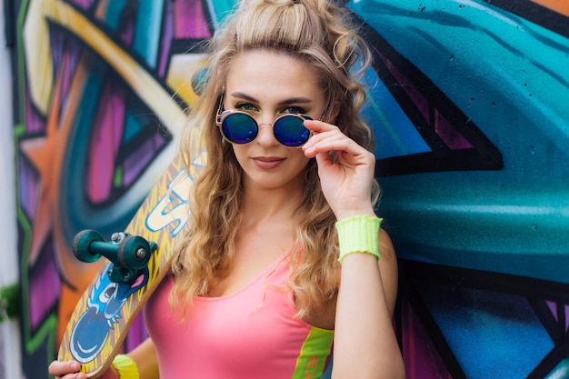 Piękna młoda blond kobieta z okularami przeciwsłonecznymi w pobliżu ściany z graffiti