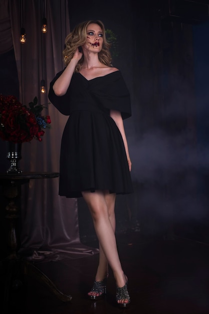 Zdjęcie piękna młoda blondynka w czarnej sukni z halloween makijaż i krwawą twarz sztuki, wnętrza vintage