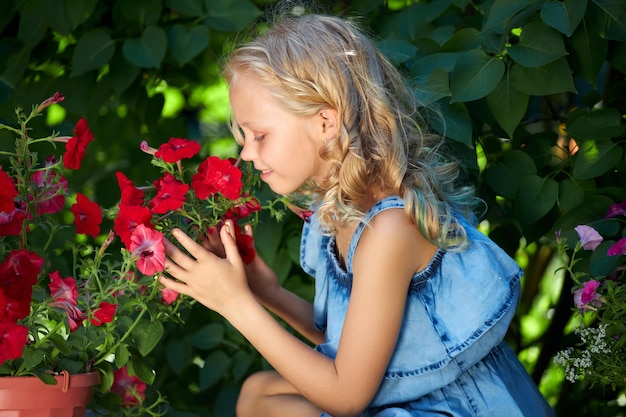 Piękna młoda blondynka w niebieskiej sukience zajmuje się kwiatami w ogrodzie