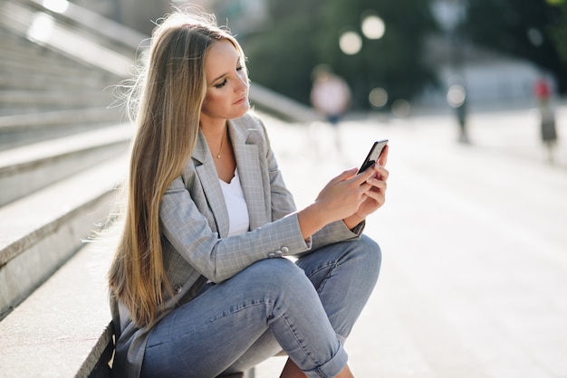 Piękna młoda blondynki kobieta patrzeje jej smartphone.