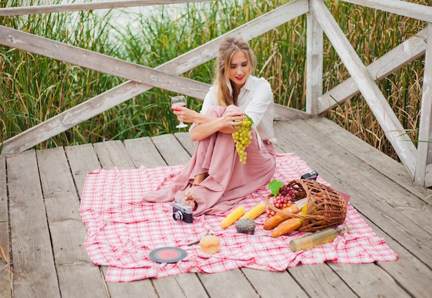 Piękna Młoda Blondynki Kobieta W Roczników Retro Ubraniach Ma Pinkin Na Drewnianym Molu Samotnie. Piknik W Stylu Francuskim Na świeżym Powietrzu