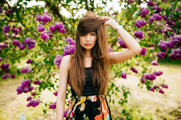 Piękna młoda brunetki dziewczyna w mody sukni pozuje w kwitnienie parku.