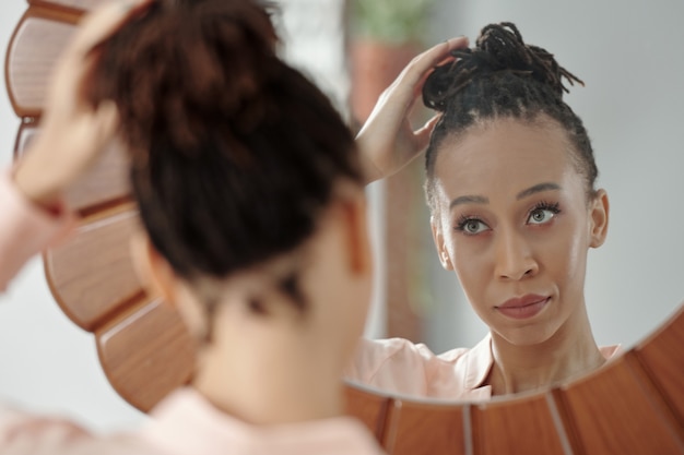 Piękna młoda czarna kobieta, patrząc w lustro i robiąc kok