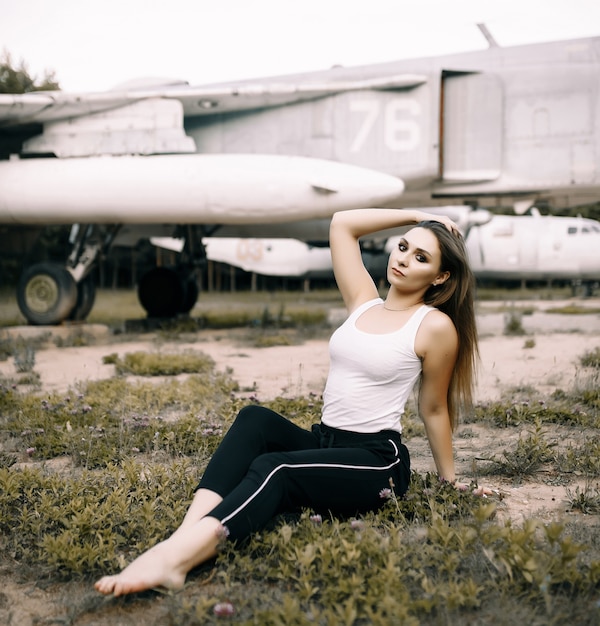 Piękna młoda dziewczyna brunetka stoi na przestrzeni starych samolotów wojskowych