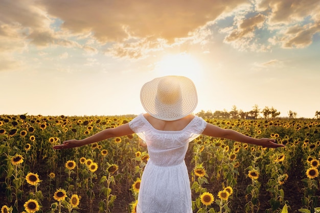 Piękna młoda dziewczyna cieszy się naturę na polu słoneczniki przy zmierzchem
