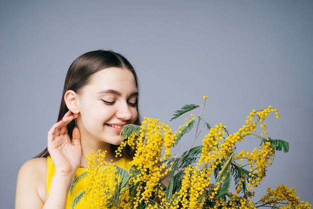 Piękna młoda dziewczyna pachnąca pachnącą żółtą mimozą, uśmiechnięta, ciesząca się wiosną