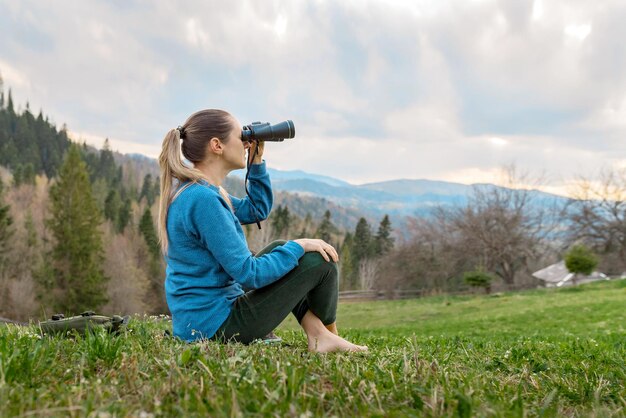 Piękna młoda dziewczyna patrząca przez lornetkę w przyrodzie w górach
