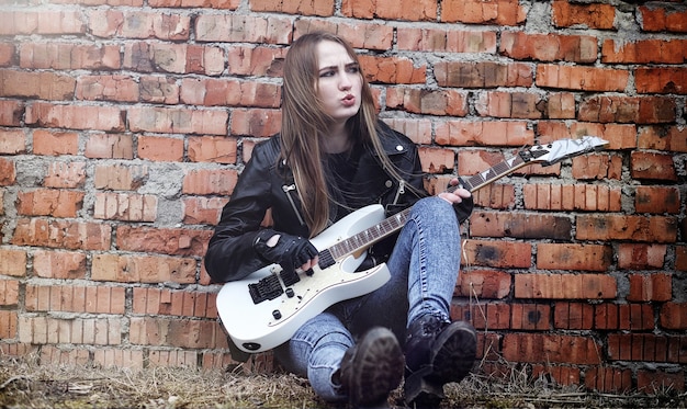 Piękna młoda dziewczyna rocker z gitarą elektryczną. Dziewczyna muzyk rockowy w skórzanej kurtce z gitarą śpiewa. Solista zespołu rockowego gra na gitarze i krzyczy do mikrofonu.