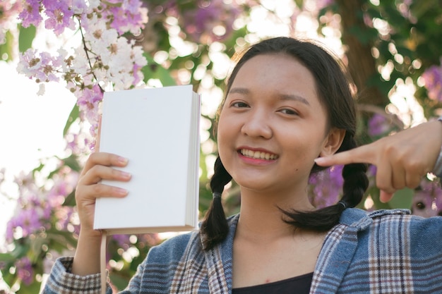 Piękna młoda dziewczyna trzyma białą książkę z fioletowym kwiatem.
