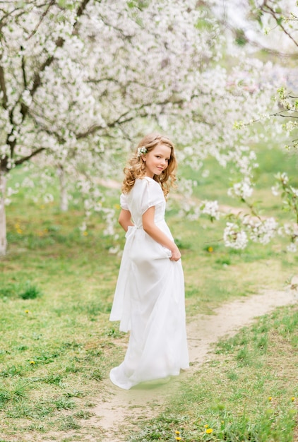 Piękna młoda dziewczyna w białej długiej sukni w kwitnącym wiosennym ogródzie