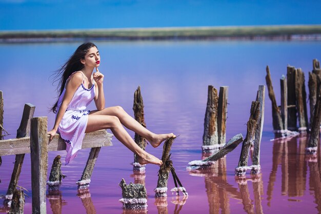 Piękna młoda dziewczyna w długiej białej sukni, pozowanie na słone różowe jezioro.