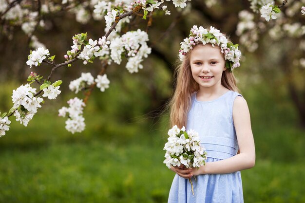 Piękna, młoda dziewczyna w niebieskiej sukience w ogrodzie z kwitnącymi jabłoniami. Uśmiechnięta dziewczyna, zabawę i ciesząc się