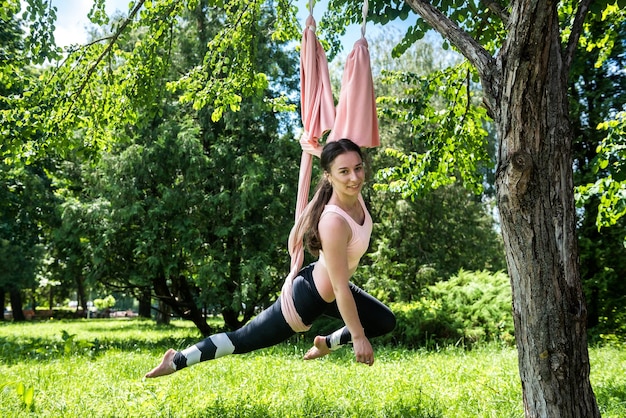 Piękna młoda dziewczyna w odzieży sportowej na naturze rozciąga się na hamaku powietrznym Koncepcja jogi latania w przyrodzie na zewnątrz