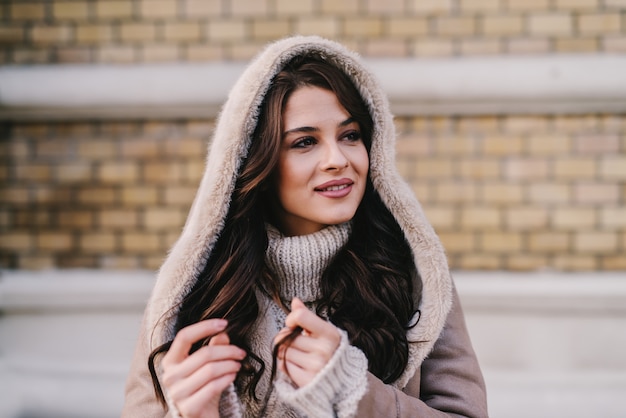 Piękna, młoda dziewczyna w płaszcz zimowy stojąc na ulicy i ciesząc się w miły zimowy dzień. Odwracając wzrok z uśmiechem na twarzy.