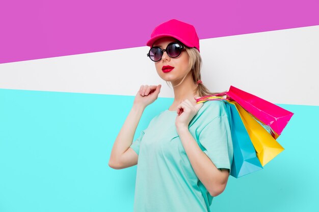 Piękna młoda dziewczyna w różowej czapce i niebieskiej koszulce z torby na zakupy na fioletowym i niebieskim tle.
