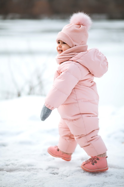 Piękna młoda dziewczyna w różowym kombinezonie w śnieżnym parku zimowym