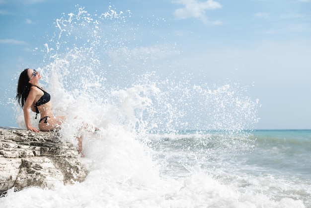 Piękna młoda dziewczyna w seksownym stroju kąpielowym na białej skale nad morzem w sprayu z fal