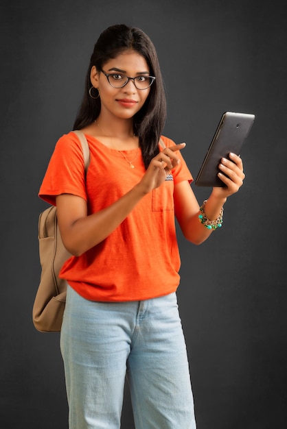 Piękna młoda dziewczyna z plecakiem przy użyciu telefonu komórkowego lub smartfona na szarym tle