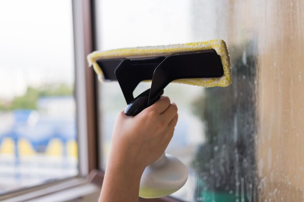 Piękna młoda gospodyni w odzieży roboczej mycie okien przez profesjonalne narzędzia w domu.