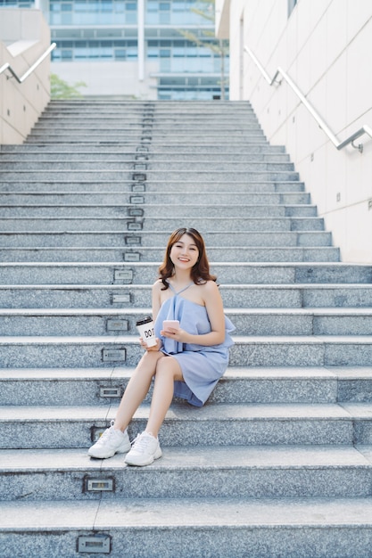 Piękna Młoda Kobieta Azji Siedzi Na Zewnątrz Schody I Przy Użyciu Smartfona. Styl życia Współczesnej Kobiety.