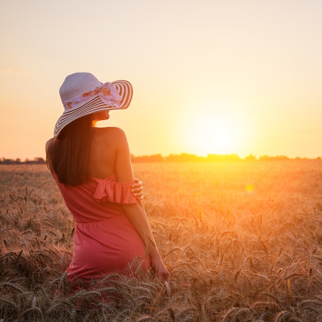 Piękna młoda kobieta, ciesząc się na zewnątrz na polu pszenicy na zachód słońca