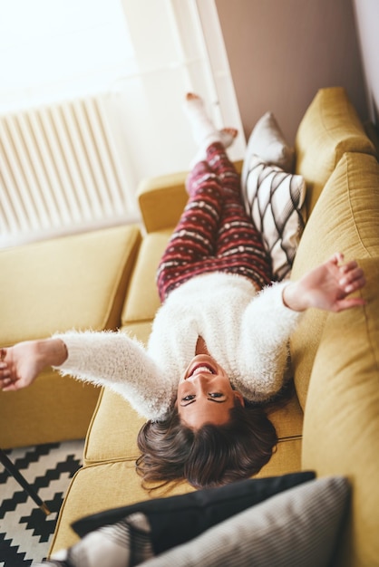 Zdjęcie piękna młoda kobieta cieszy się w salonie. leży na kanapie z rękami za głową.