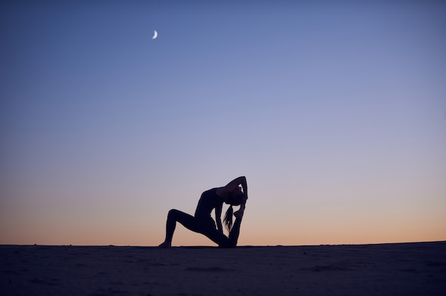 Piękna młoda kobieta ćwiczy jogę asan Król Gołąb pozować rajakapotasana na pustyni w nocy