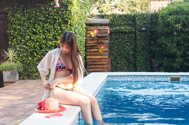 Piękna młoda kobieta dostosowując jej bikini z nogami schowanymi do basenu.