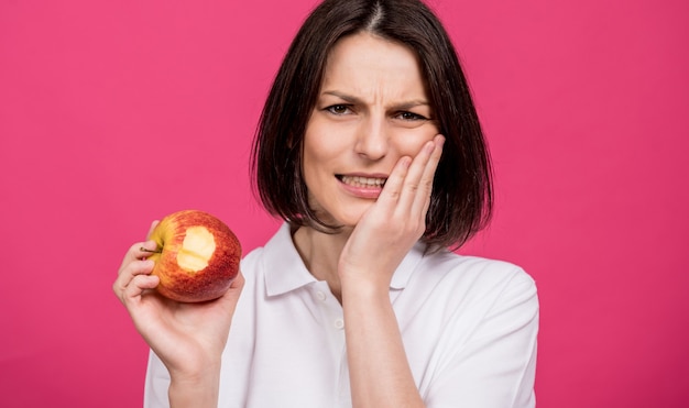 Piękna młoda kobieta gryzie duże jabłko i boli ją ząb