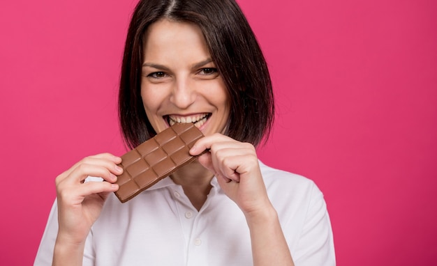 Piękna młoda kobieta gryzie tabliczkę czekolady