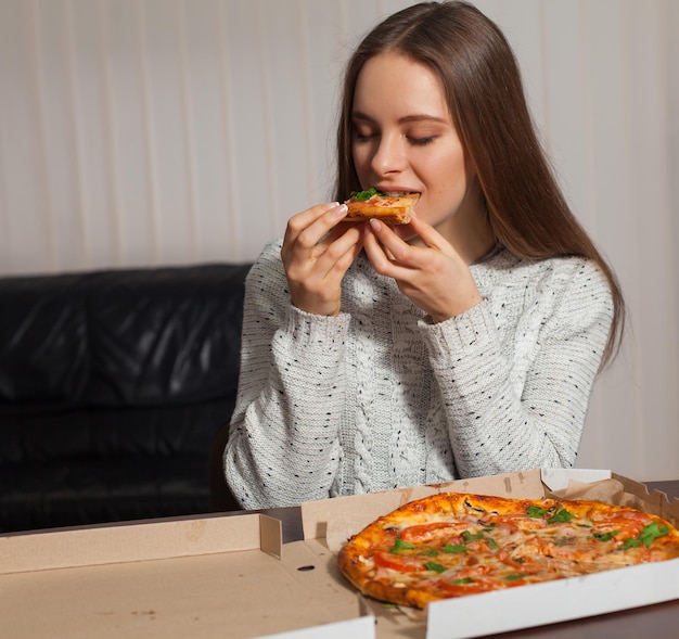 Piękna młoda kobieta je pizzę w biurze