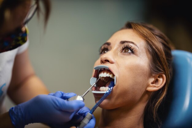 Piękna młoda kobieta jest u dentysty. Siedzi na fotelu dentystycznym, a dentysta zakłada na jej zęby aparat ortodontyczny, zakładając estetyczne samonastawne zamki językowe.