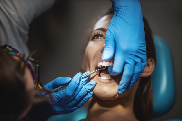 Piękna Młoda Kobieta Jest U Dentysty. Siedzi Na Fotelu Dentystycznym, A Dentysta Zakłada Na Jej Zęby Aparat Ortodontyczny, Zakładając Estetyczne Samonastawne Zamki Językowe.