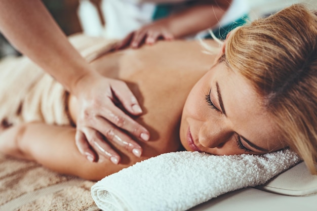 Piękna młoda kobieta leży na stole do masażu i otrzymuje zdrowy masaż pleców przez młodą terapeutkę w centrum spa.