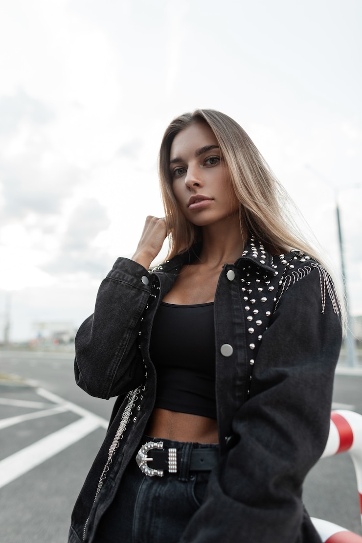 Zdjęcie piękna młoda kobieta model z blond włosami z ładną buzią w moda czarna kurtka dżinsowa i czarny top t-shirt z czarnymi dżinsami z paskiem spacery po mieście